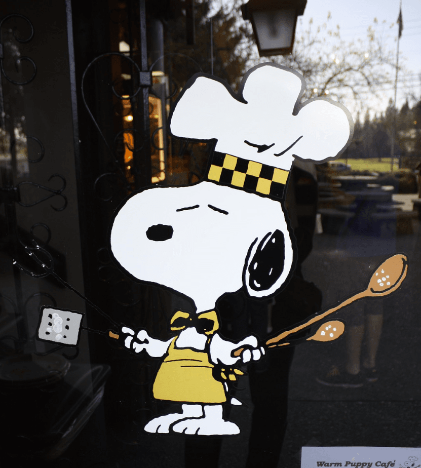 The Peanuts cartoon character Snoopy is shown dressed as a chef, ready to serve up food.